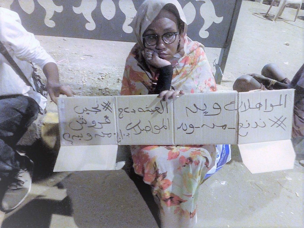 مواطنة ترفع لافتة احتجاج بموقف البصات: “نجيب قروش من وين؟”